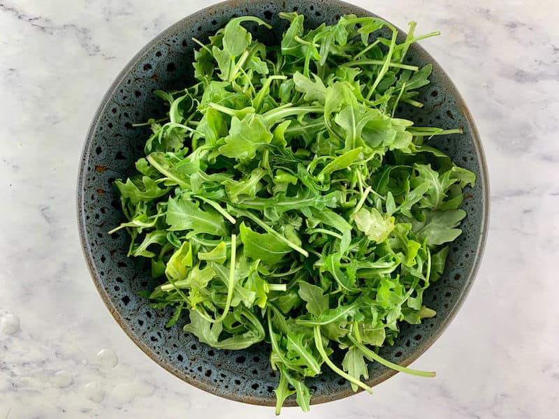 Washed arugula in a salad in dark grey patterned salad bowl.
