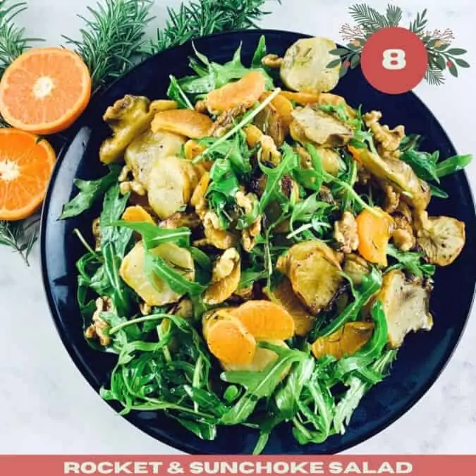 Rocket and Sunchoke Salad in a dark blue bowl with mandarin halves and rosemary sprigs in top left corner and with Xmas text overlay.