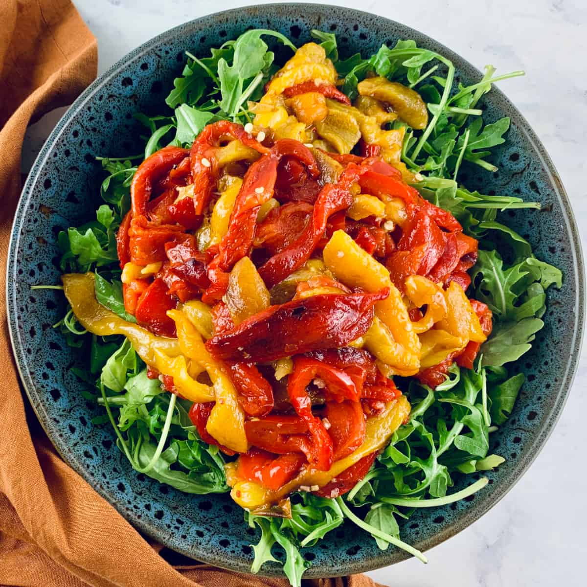 COLOURFUL ROASTED BELL PEPPER SALAD IN A GLASS BOWL WITH SERVING SPOONS ON THE SIDE