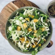 Fennel and Orange Salad in a deep ceramic bowl on a wooden board with mustard in a bowl on top right corner.