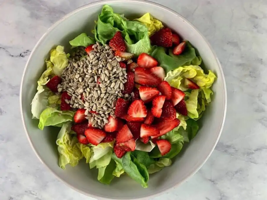 Lettuce salad with strawberries in a white bowl.