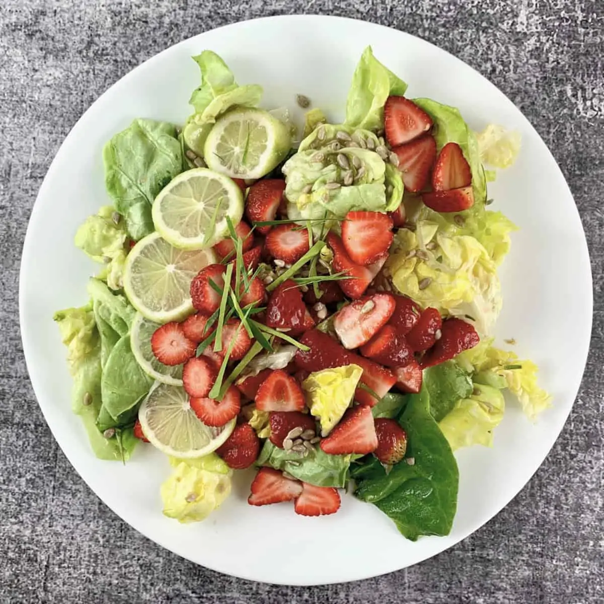 Lettuce salad with strawberries in a white salad platter with lime garnish, square view.