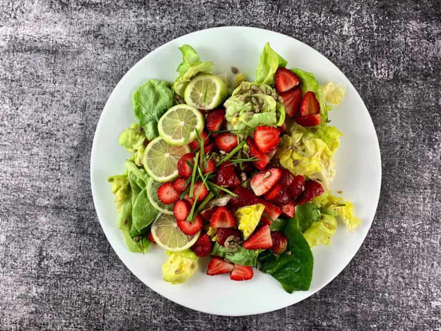 Lettuce salad with strawberries in a white salad platter with lime garnish in landscape view.
