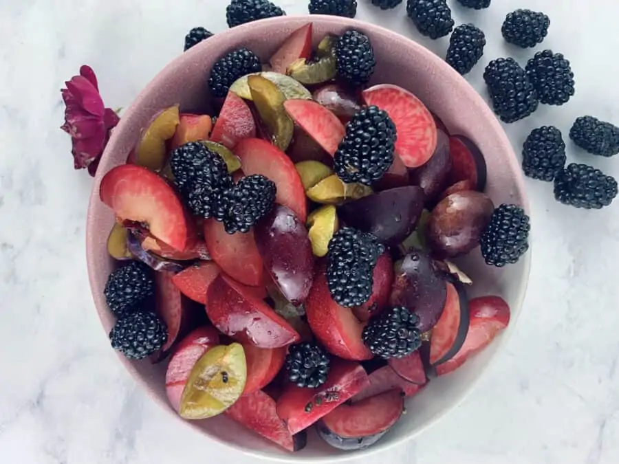 Plum Salad with Blackberries in a pink bowl with blackberries scattered on the side.