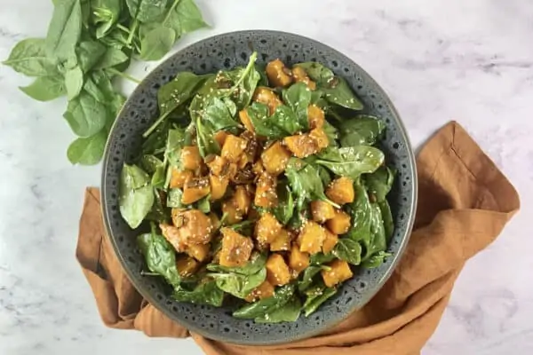 Pumpkin salad on a grey patterned shallow bowl with baby spinach in top left hand corner and orange linen napkin at the bottom.