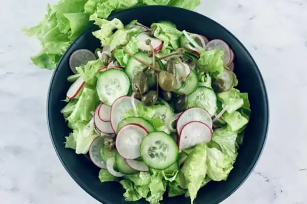 Radish Green Salad in a black bowl, garnished with caper berries and lettuce leaves up top.