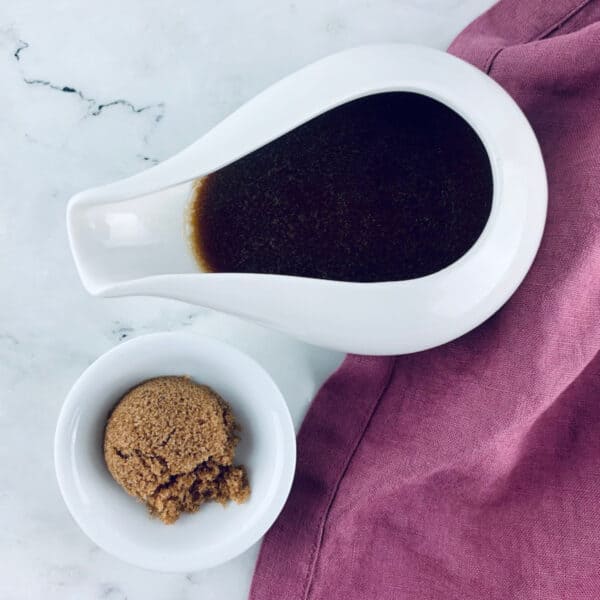 Sweet balsamic vinaigrette in a small white jug with brown sugar in a small white bowl underneath and a pink linen napkin on the right.
