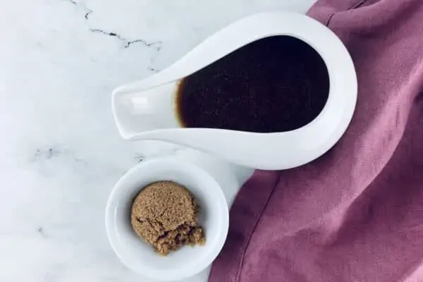 Sweet balsamic vinaigrette in a small white jug with brown sugar in a small white bowl underneath and a pink linen napkin on the right.