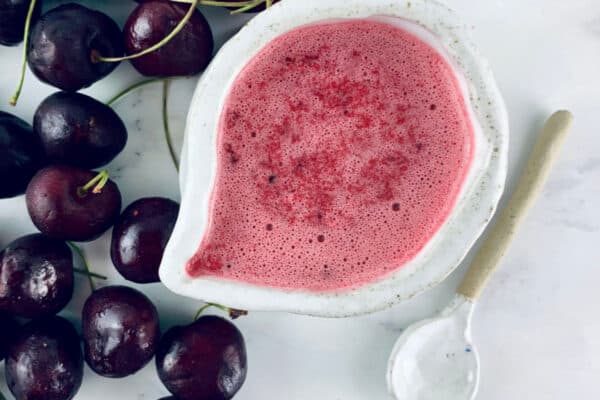 cherry vinaigrette in a white jug with cherries on the left and a spoon on the right.