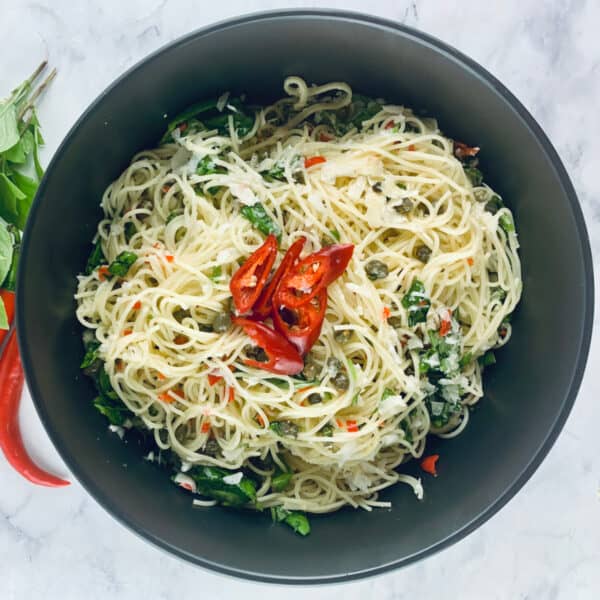 Lemon capellini salad in a black bowl with red. chillies and basil sprigs on the left hand side.