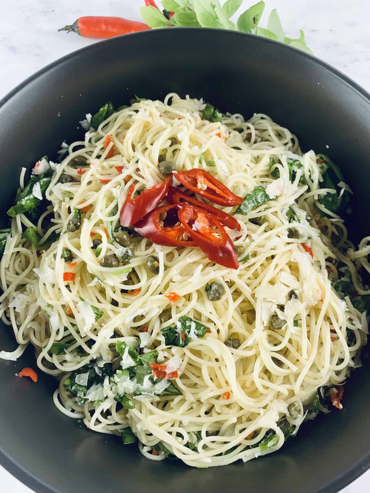 Lemon capellini salad in a black bowl with red. chillies and basil sprigs on the top.