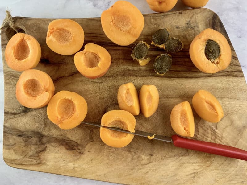 Removing the pit and cutting apricots into half then quarters with a red knife.