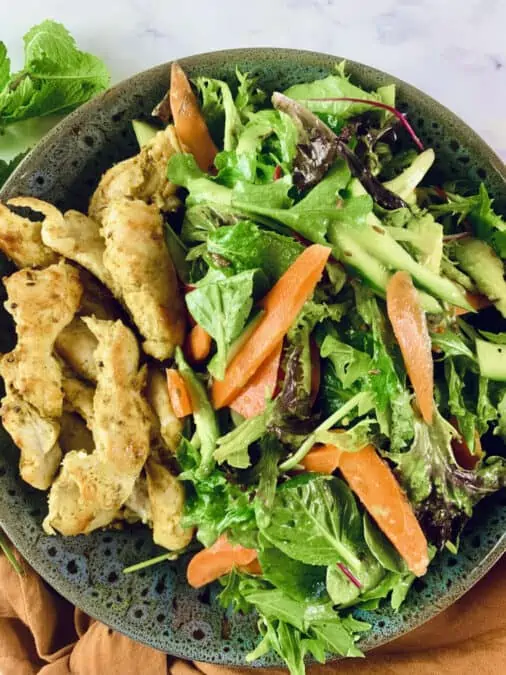 Keto Curry Chicken Salad in a dark grey patterned bowl with an orange linen napkin at bottom right corner and mint leaves on left.