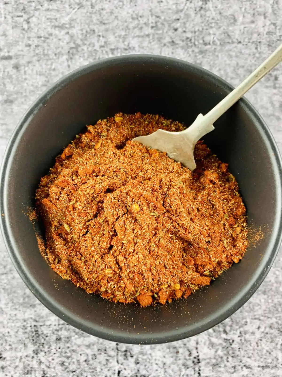 Keto-friendly taco seasoning in a black bowl with a silver spoon.