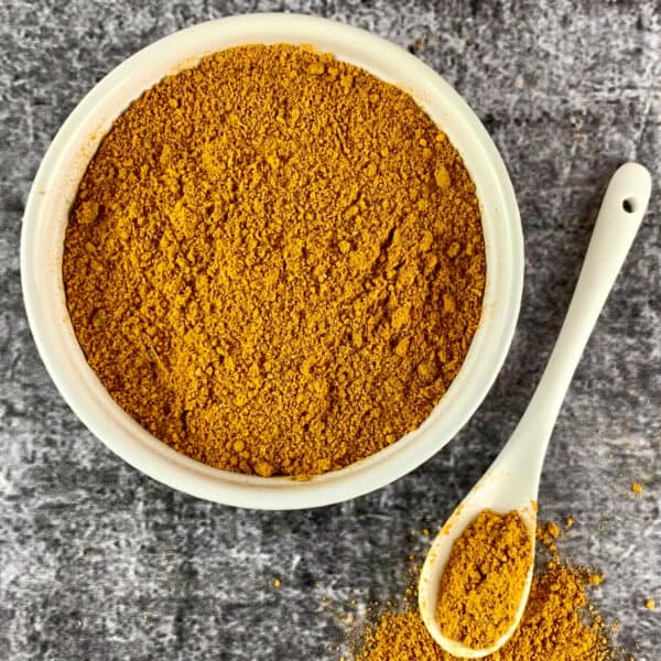 Madras Curry Powder in a white bowl with a teaspoon of powder on the side.