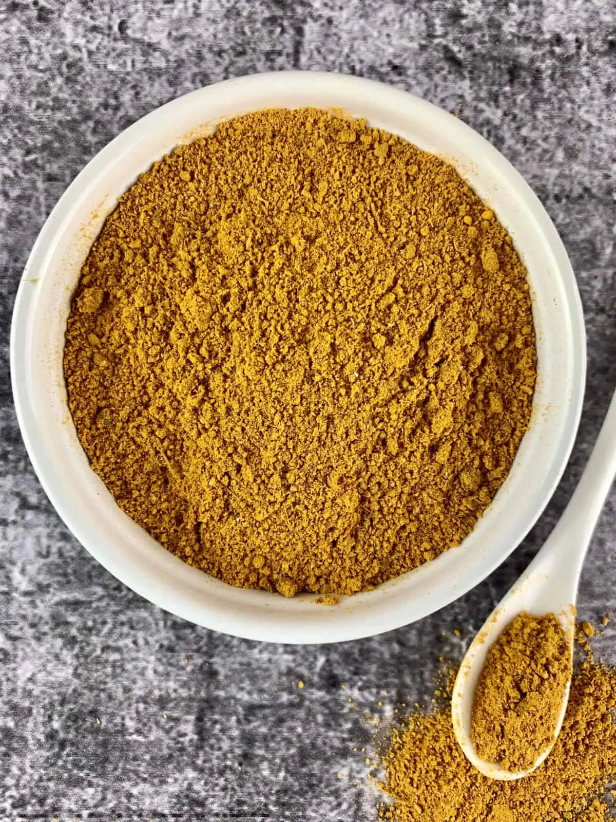 Madras Curry Powder in a white bowl with a teaspoon of powder on the side.