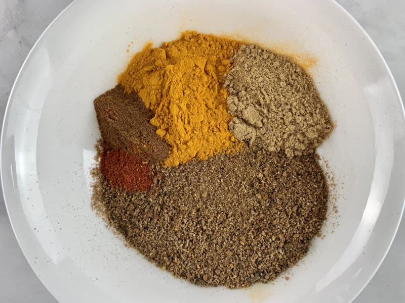 Adding all Madras spices to a white bowl.