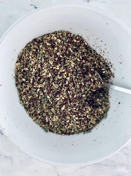 Mixing za'atar subsitute ingredients in a white bowl.