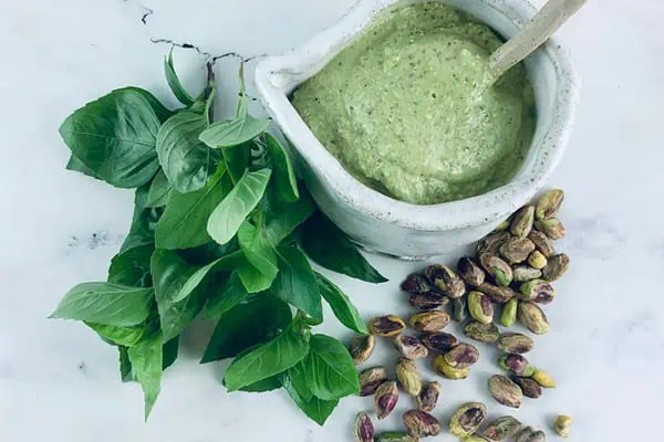 Pistachio dressing in a ceramic jug and spoon with pistachios and basil sprigs on the side.
