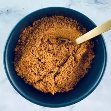 Ras el Hanout spice blend in a black bowl with a gold teaspoon.