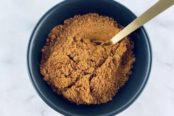 Ras el Hanout spice blend in a black bowl with a gold teaspoon.