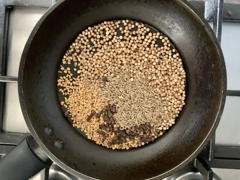 Whole madras curry spices in a pan on the stove.