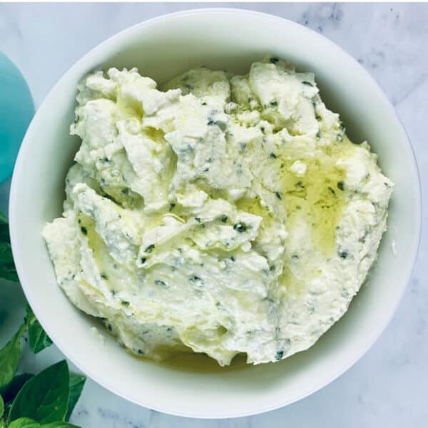 Whipped feta in a bowl with fresh basil and olive oil in an aqua bottle on top.