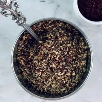 Za'atar substitue in a silver bowl with a spoon, sumac in a small white bowl on the right.