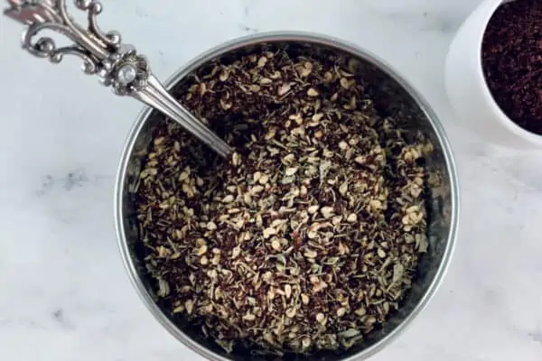 Za'atar substitue in a silver bowl with a spoon, sumac in a small white bowl on the right.