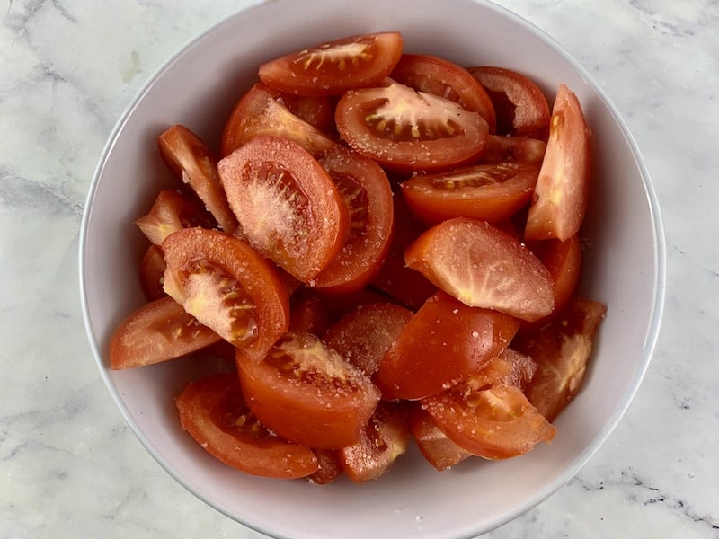 Tomato wedges in a white bowl with salt to sweeten them.