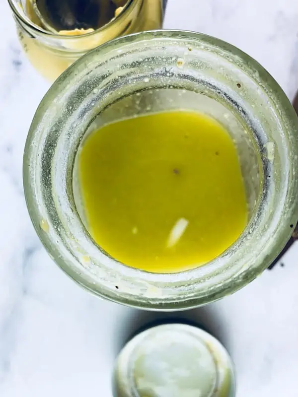 Shaken French mustard vinaigrette in a glass jar with ingredients scattered around.