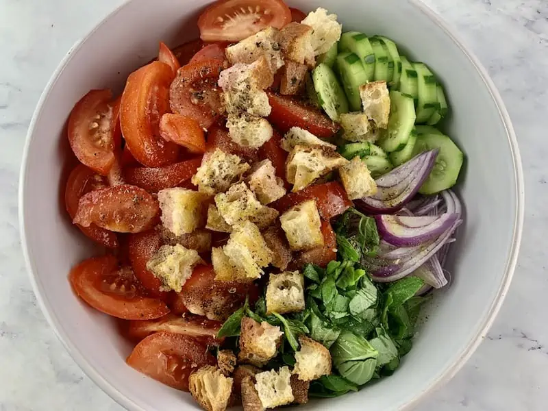 Prepared Panzanella Toscana ingredients in a white mixing bowl.