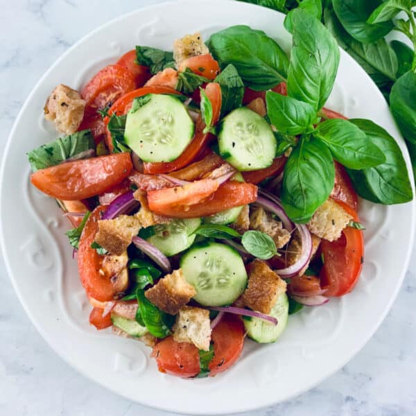 Panzanella Toscana Salad in a white bowl with basil sprigs on the top right.