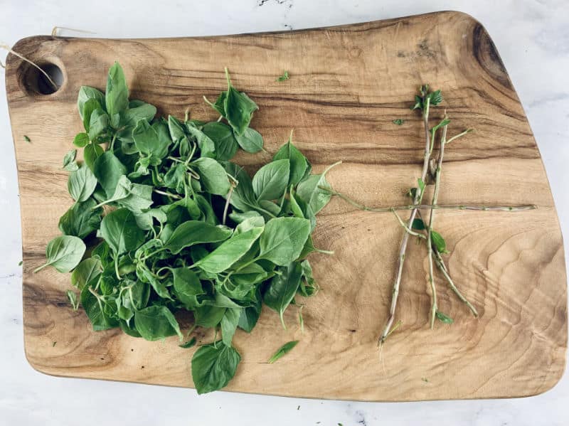 Basil leaves stripped from stems on a wooden board.