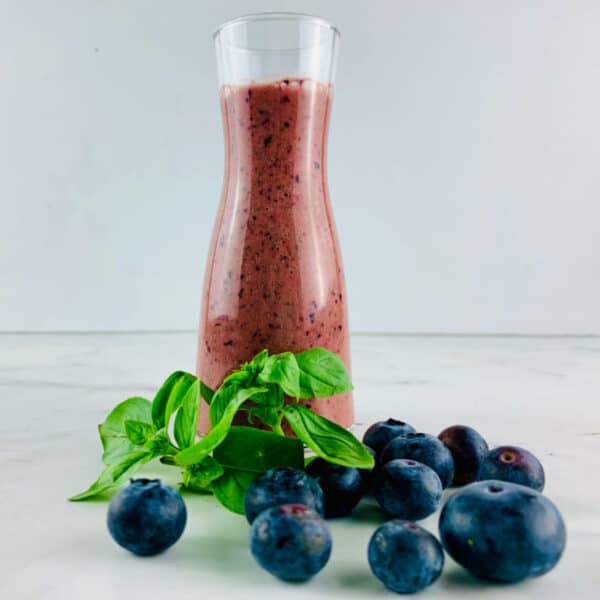Blueberry salad dressing in a glass bottle with fresh blueberries and basil sprigs in front.