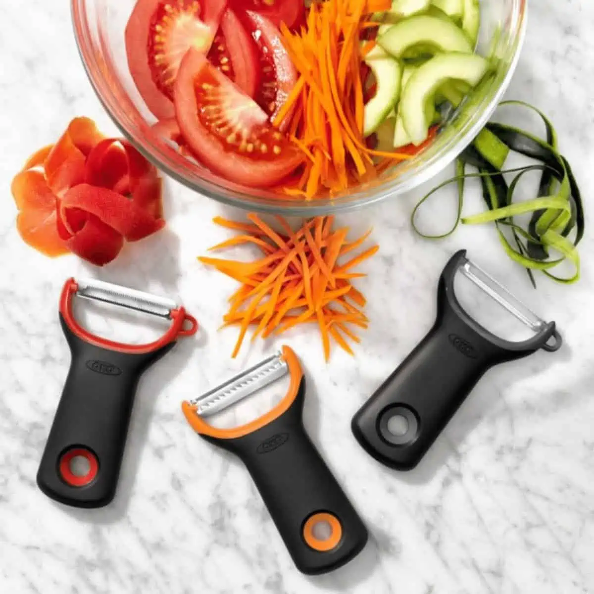 3 different types of peelers with peeled vegetable examples above them and a bowl of cut veggies on top.
