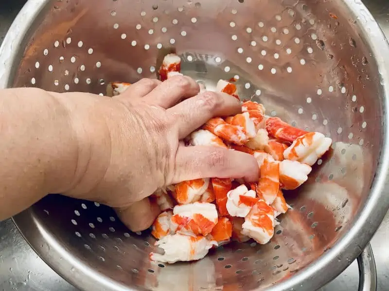 Hand squeezing the water out prawns in a colander in the sink.