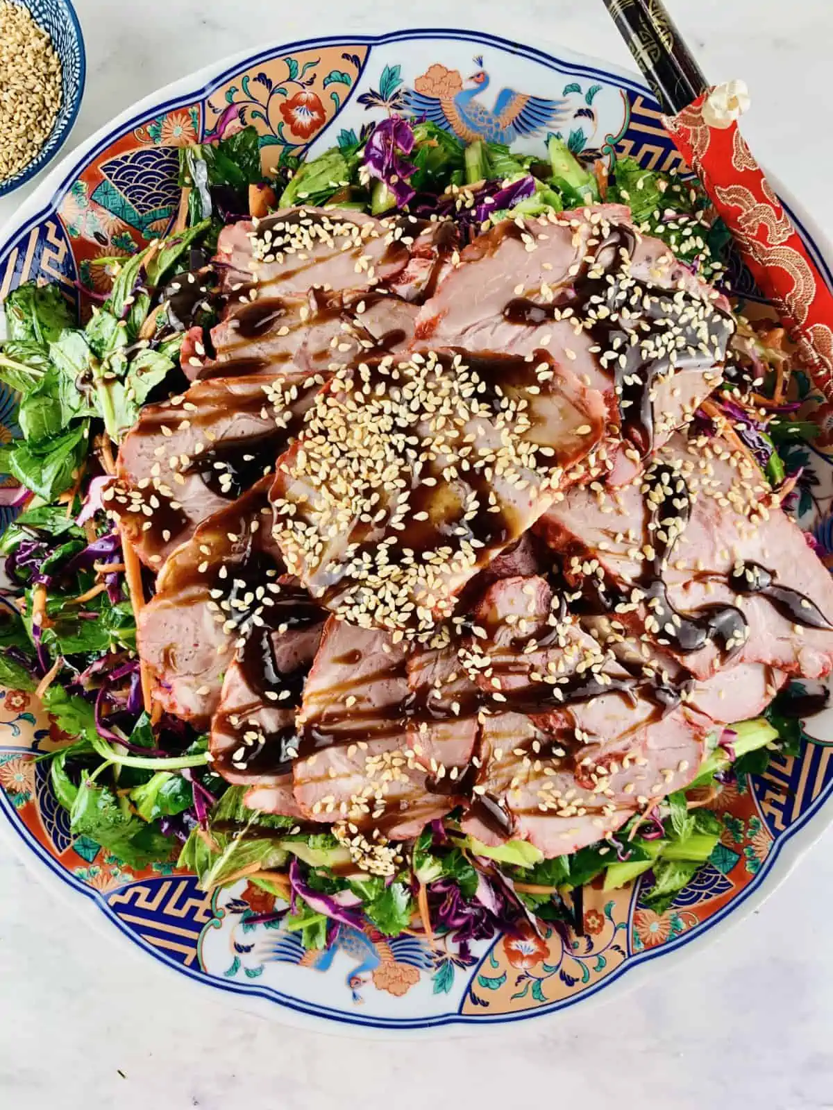 Asian Pork Salad on an Asian style platter with red chopsticks on right & sesame seeds on left.