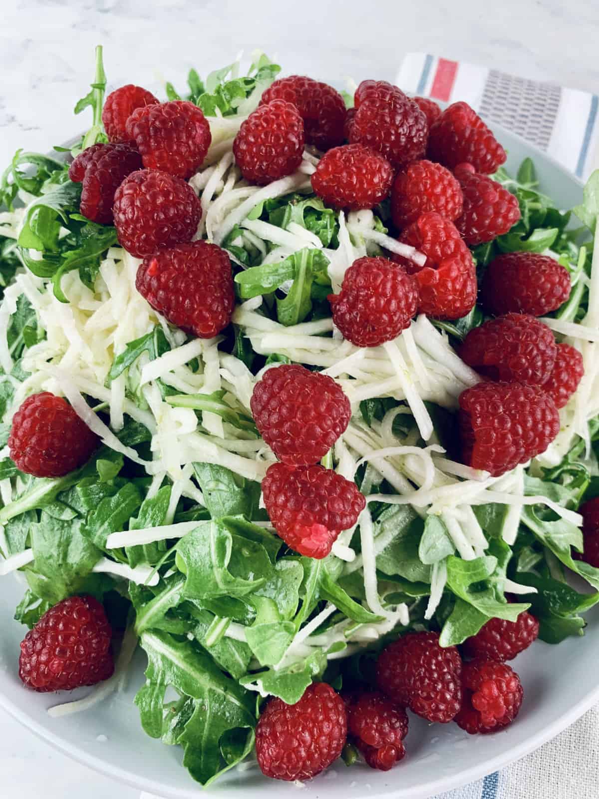 A close-up of Kohlrabi Raspberry Salad on a blue plate with striped tea towel underneath.