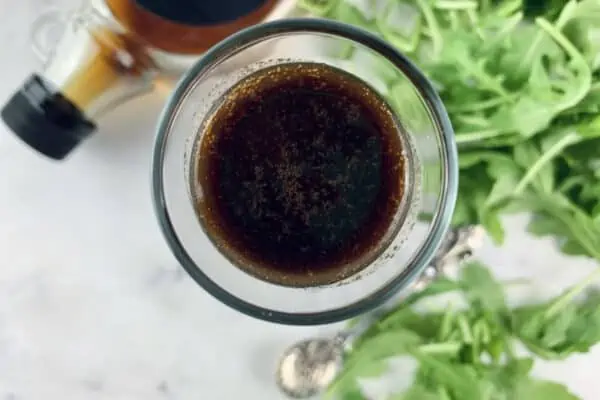 Maple balsamic dressing in a glass bottle with maple and rocket on the side.