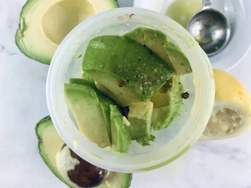 Avocado mayo ingredients in a blender with ingredients around.