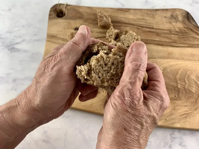 Hands breaking apart barley rusks over a wooden board.