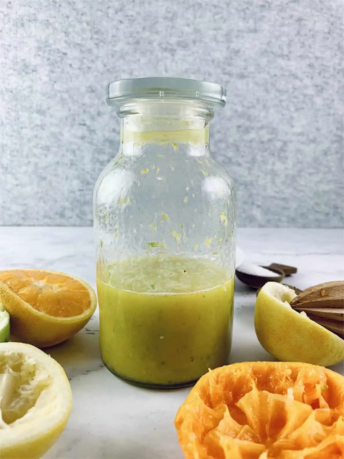 Citrus salad dressing in a glass bottle with ingredients scattered around.