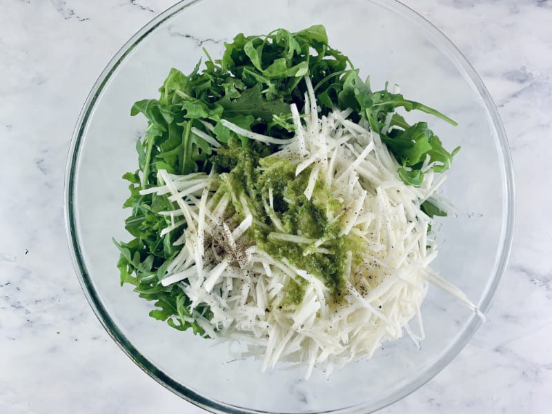 Dressing on grated kohlrabi and rocket in a glass bowl.