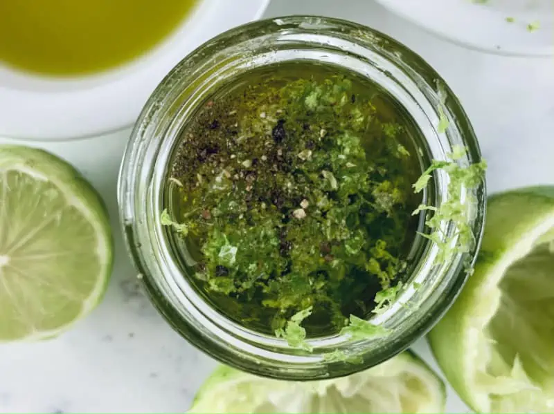 Lime vinaigrette ingredients in a glass jar with other ingredients scattered about.