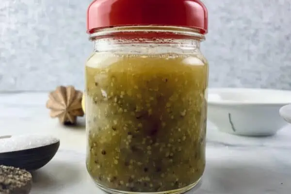 Orange mustard dressing in a glass jar with a red lid with ingredients scattered about.