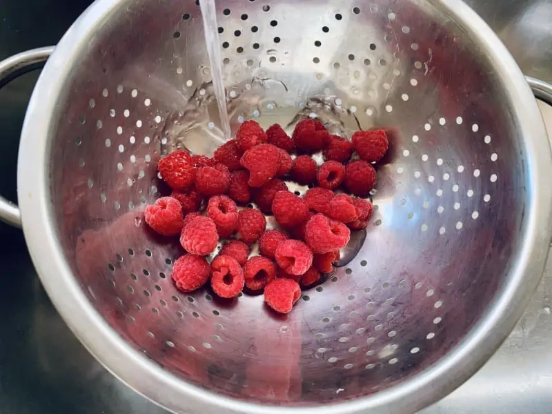 Berries in a colander being rinsed under water in the sink.