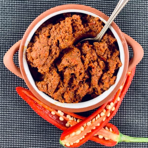 Moroccan roasted harissa paste in a clay pot with a spoon and chillies at the bottom.