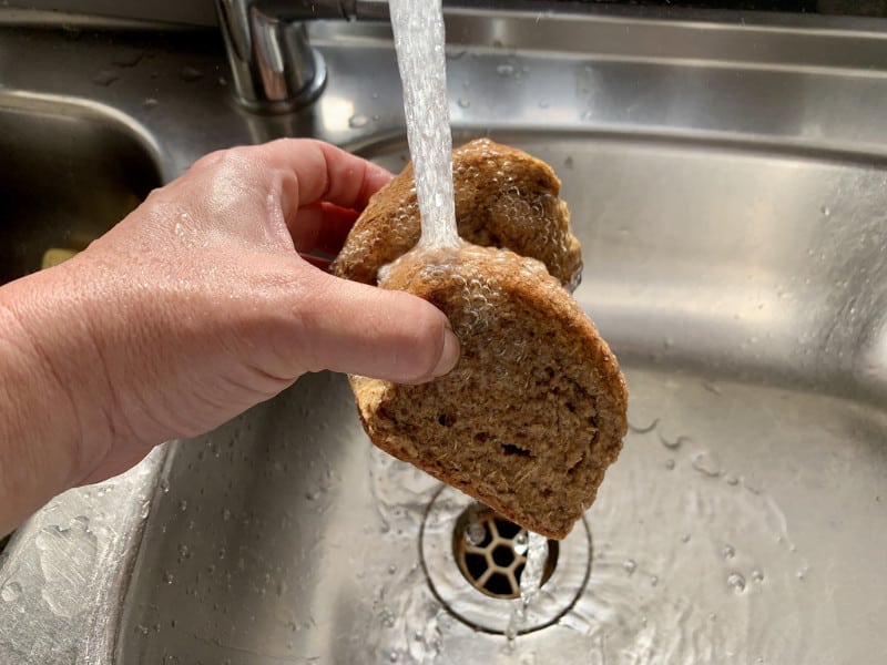 Hands wetting barley rusks under cold water in the sink.
