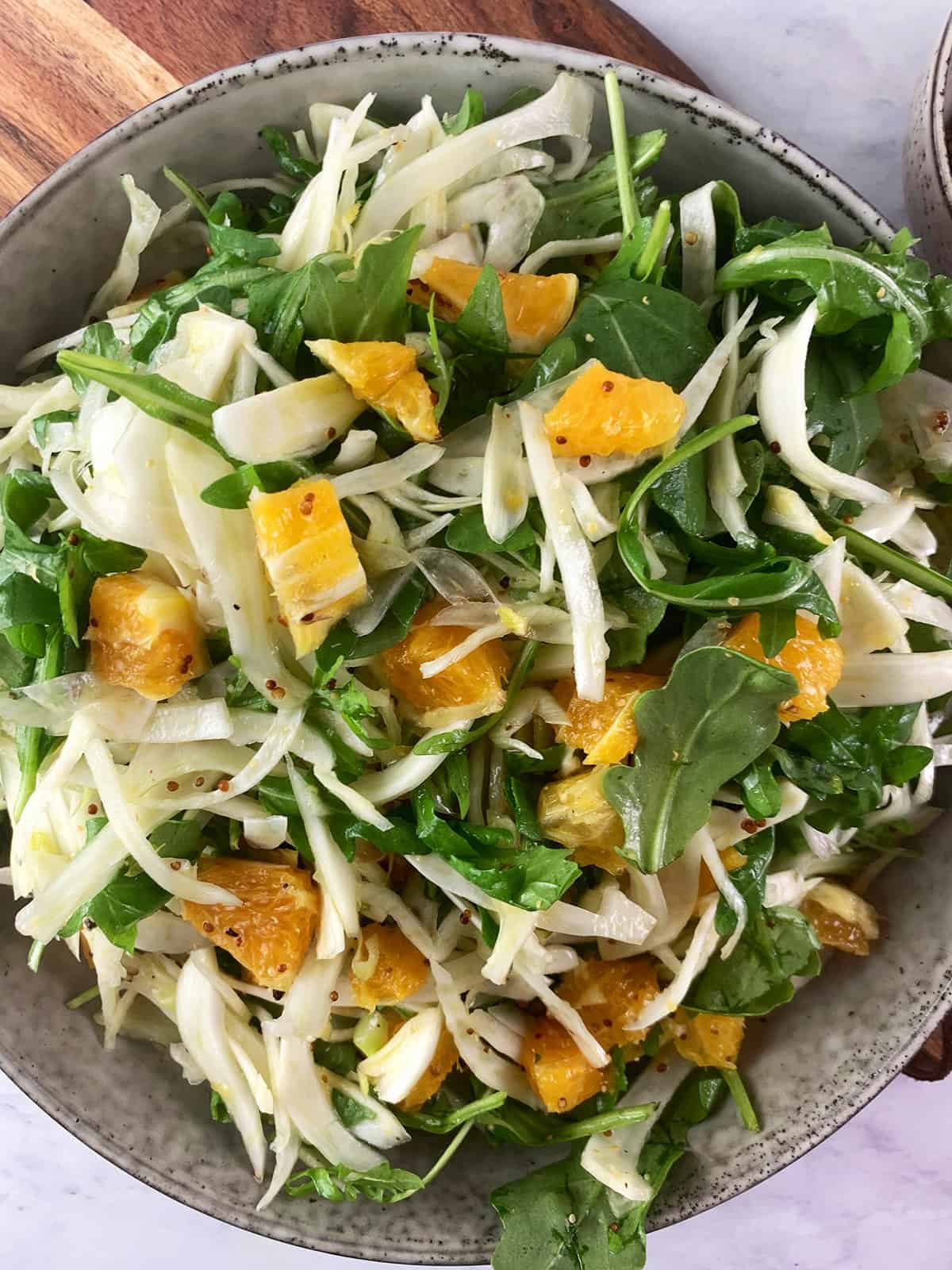 A close up of Fennel and Orange Salad in a deep ceramic bowl on a wooden board.